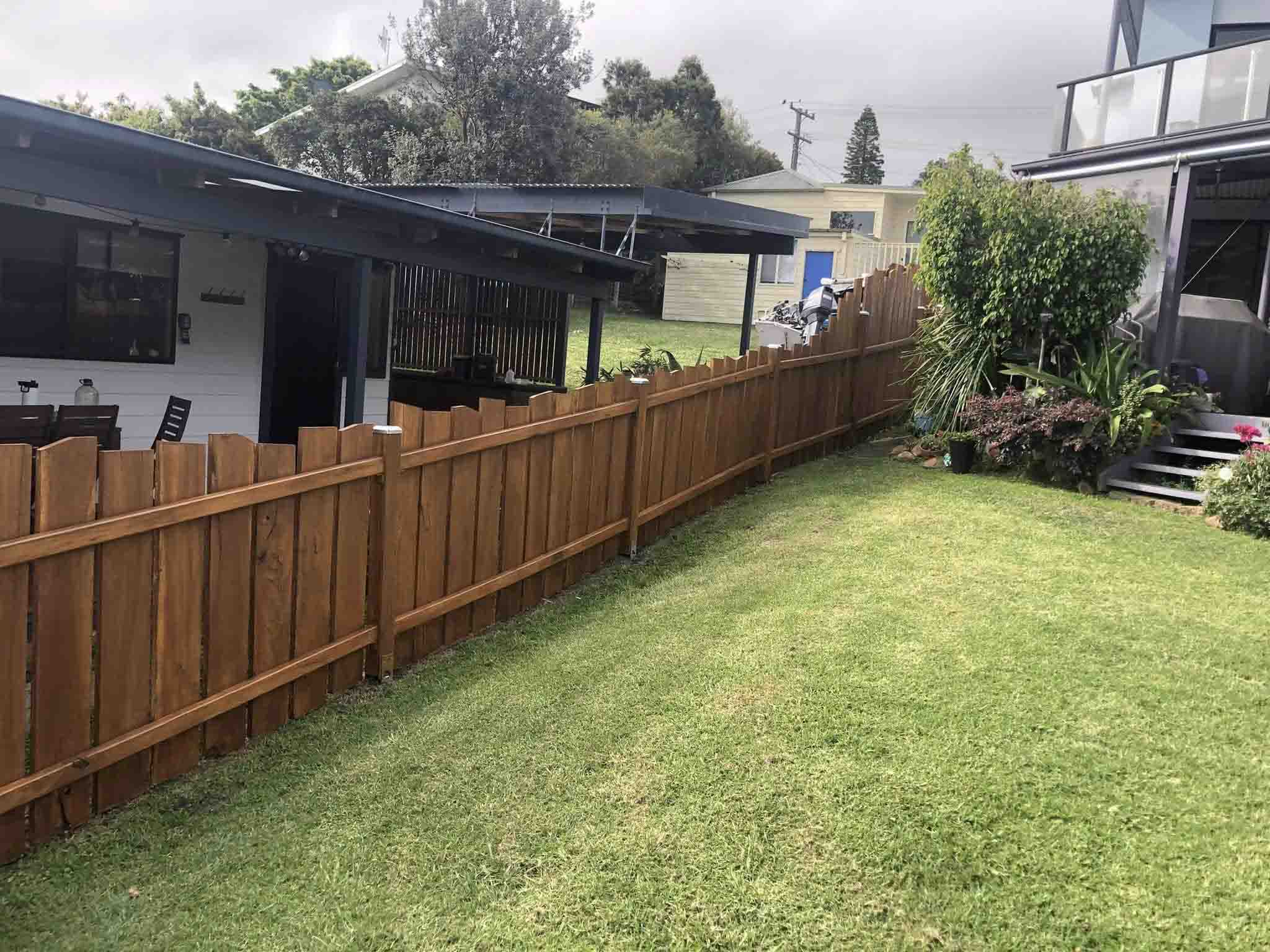 Stained timber paling fence along a sloping backyard lawn